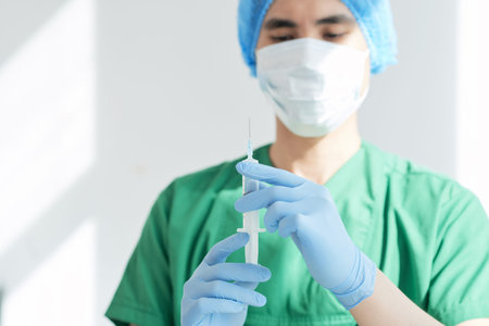 Asian health professional in mask holding syringe and preparing for injection while working in hospitalの写真素材