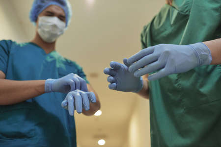 Anonymous men in surgeon uniform putting on latex gloves while standing in hospital hallwayの写真素材
