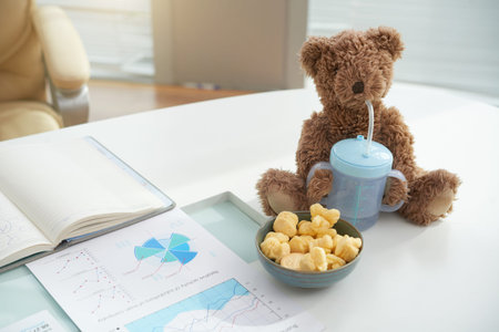 Table with bowl of sweet snack and kid toy with bottle of water on table of working office workerの写真素材