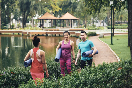 Vietnamese sporty people with yoga mats coming to outdoor yoga class