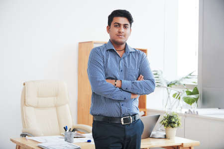 Confident young Indian businessman standing with his arms folded and looking at cameraの写真素材