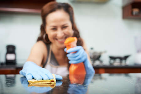Smiling housewife cleaning table surface in kitchen with sprayの写真素材