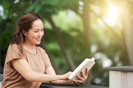 Mature Asian woman enjoying reading a book outdoorsの写真素材