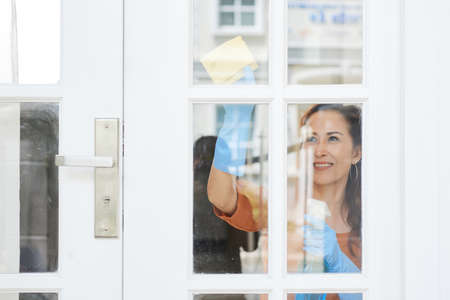 Smiling mature housewife cleaning door with detergentの写真素材