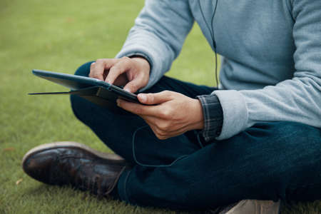 Anonymous guy in casual outfit sitting on green lawn and using modern tabletの写真素材