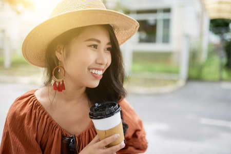Pretty young Asian woman drinking take-out coffee outdoorsの写真素材