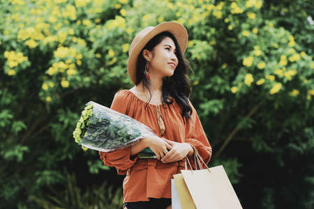 Very attractive smiling young Asian woman standing outdoors with bouquet of flowersの写真素材