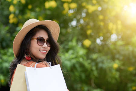 Portrait of cheerful young woman in sunglasses holding shopping bagsの写真素材