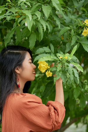 Pretty young Vietnamese woman smelling bright yellow flowerの写真素材