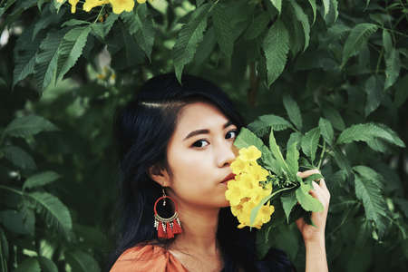 Portrait of attractive unsmiling young woman posing with flowers and looking at cameraの写真素材