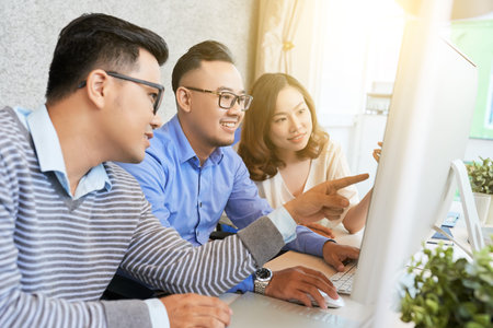 Young Asian men and woman in light office watching computer together while working on business plan...