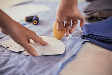 Closeup shot of hands of anonymous tailor using piece of chalk to outline paper pattern on blue...
