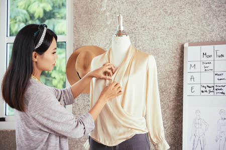 Side view of Asian female tailor creating elegant blouse on dummy while working in studioの写真素材