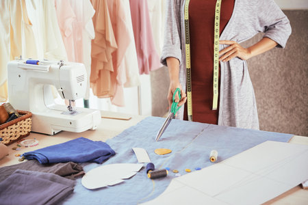 Anonymous fashion designer holding sharp scissors and standing near table with blue cloth while...