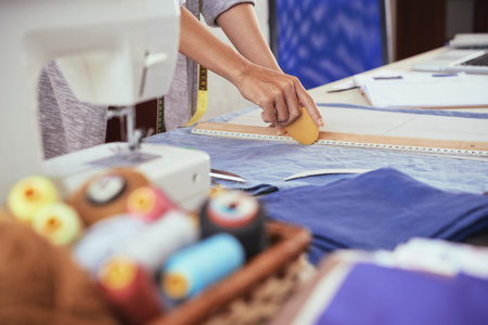 Side view of crop young female using chalk and ruler to draw line on blue fabric while working in...