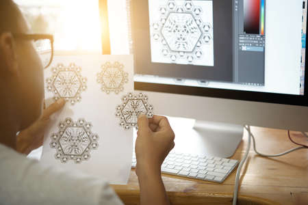 Creative designer looking at snowflakes he drawn on computerの写真素材