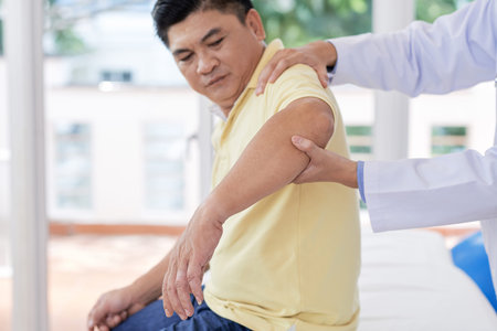 Anonymous medical practitioner examining arm of adult Asian man while working in office