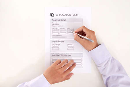 From above shot of hands of unrecognizable person using pen to fill gaps in application form on white backgroundの写真素材