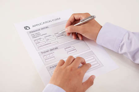 Hands of anonymous person writing down personal information in application form on white backgroundの写真素材