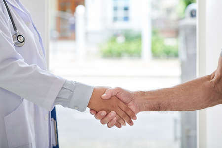 Crop shot of senior man and female doctor in uniform shaking hands during home visitの写真素材