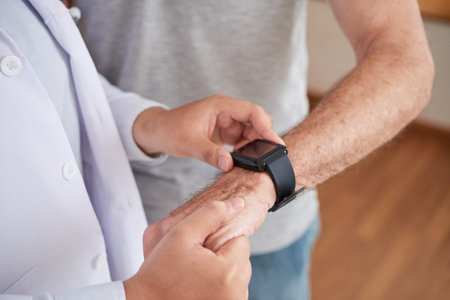 Crop shot of doctor measuring pulse of senior man with smart watch standing at homeの写真素材