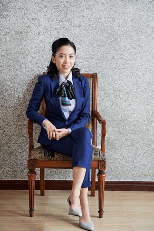 Young Asian woman in blue suit and heels sitting in armchair smiling at cameraの写真素材