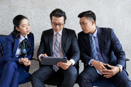 Young Asian men and woman watching tablet together working in businessの写真素材