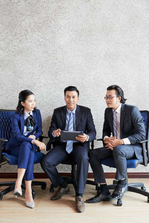 Modern adult Asian men and woman gathering together sitting on chairs and talkingの写真素材