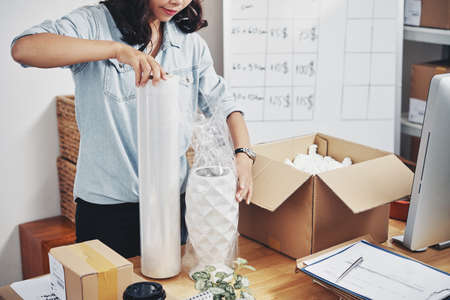 Young office worker packing beautiful vase in cardboard boxの写真素材