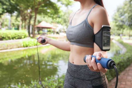 Faceless shot of slim sportswoman wearing armband and holding jumping rope in parkの写真素材