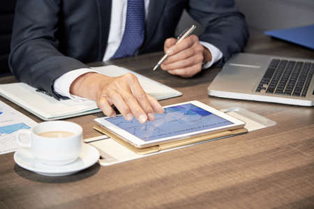 Faceless shot of anonymous formal man sitting at table in office with papers and using tabletの写真素材