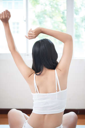 Back view of woman in white underwear sitting on bed and stretching after awakening in morningの写真素材