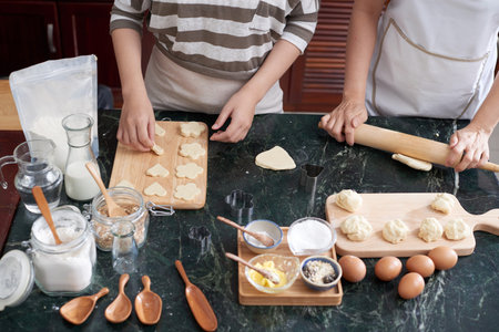 High angle view of anonymous women rolling cookie mixture and cutting out with cutters on kitchen...