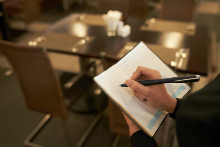 Crop shot of elegant woman writing in notepad while standing in restaurant of modern hotelの写真素材