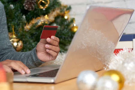 Crop man sitting at table with credit card using laptop and buying Christmas presents onlineの写真素材