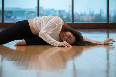 Side view of attractive Asian female lying on floor and looking at camera while dancing in stylish studioの写真素材