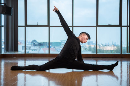 Side view of young Asian guy performing split while dancing on floor of modern studio