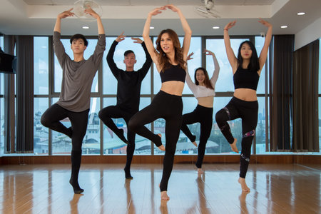 Group of slim Asian people standing on one foot and looking away while dancing in stylish studio