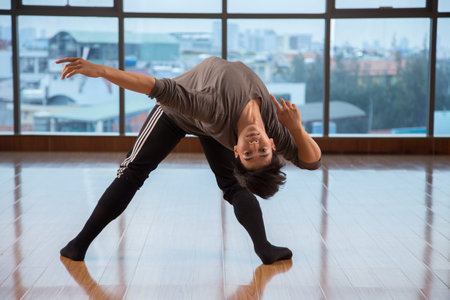 Handsome Asian guy bending back and looking at camera while dancing near window in stylish studio
