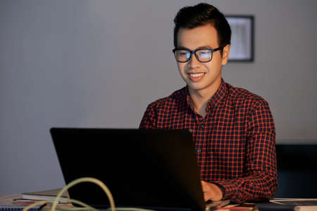 Happy Vietnamese programmer reading e-mails on laptop screenの写真素材