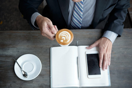 Businessman drinking coffee before writing plans and ideas in notepadの写真素材