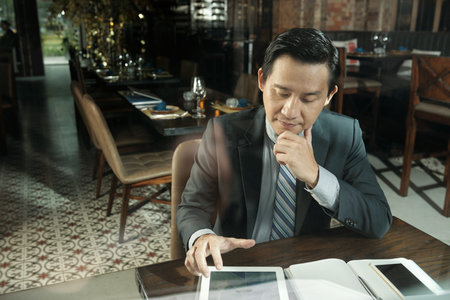 Pensive Asian business partners executive looking at diagram of company income on table screen when drinking coffee in restaurantの写真素材