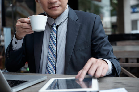 Cropped image of businessman drinking morning coffee and checking information on tablet computerの写真素材