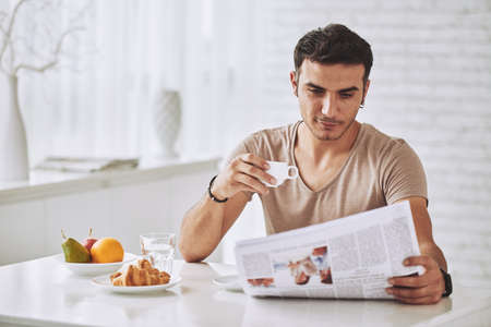 Young man enjoying breakfast and reading newspaperの写真素材