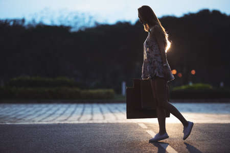 Young woman with many shopping bags walking in unlit streetの写真素材