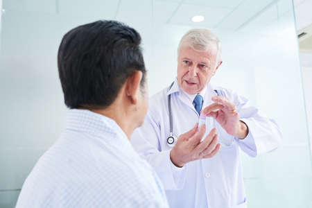 Senior medical practitioner showing container of medicine to anonymous patient and explaining how to use itの写真素材