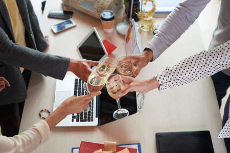 Group of colleagues toasting with champagne glasses over office table to celebrate Christmasの写真素材