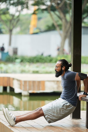 Side view of concentrated bearded Indian male athlete listening to music through earbuds while...