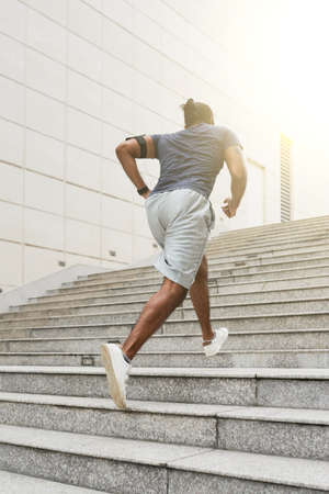 Unrecognizable athletic man in sportswear running up concrete stairs outdoors while having daily morning workout, rear viewの写真素材