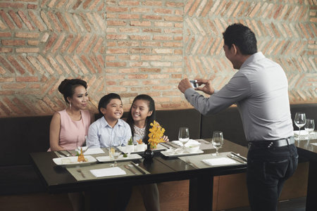Father photographing his family at the table during dinner on his mobile phoneの写真素材